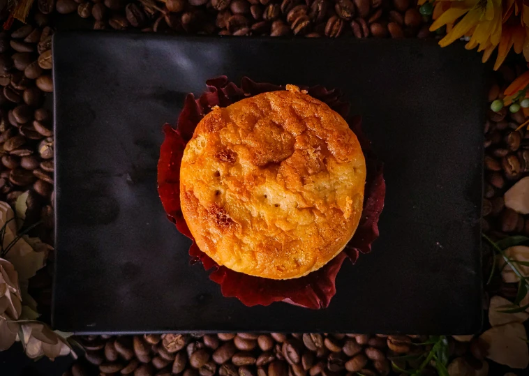 a breaded pastry sitting on a dark surface surrounded by flowers and leaves