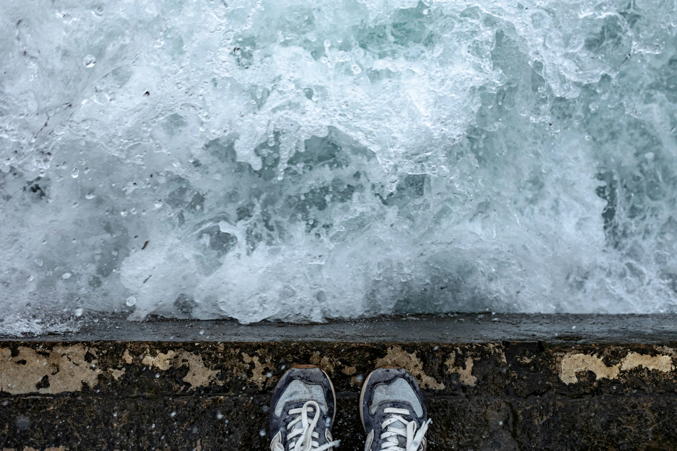 person wearing sneakers by the sea, surrounded by rough waves