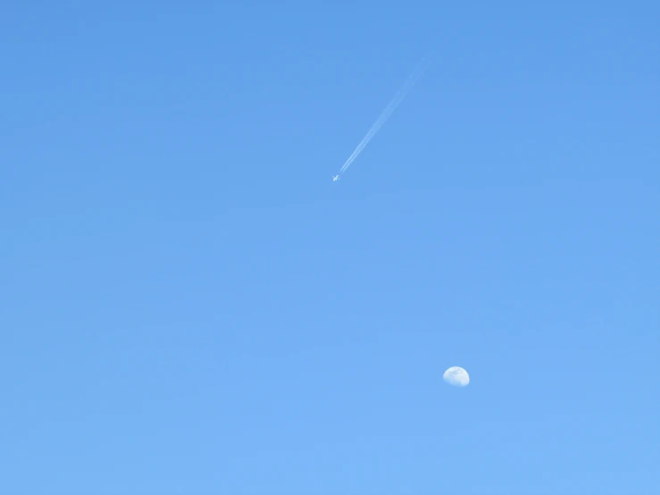 a plane flies in the sky as a half moon is seen below