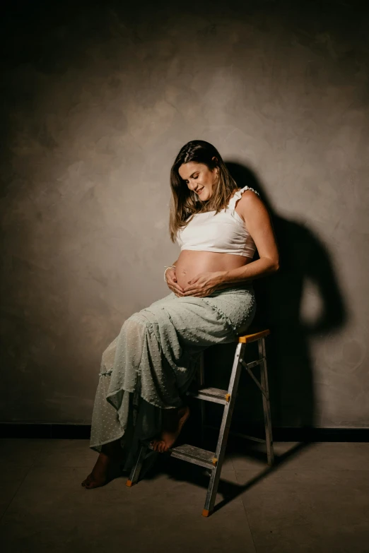 a pregnant woman sits on a chair with her stomach exposed