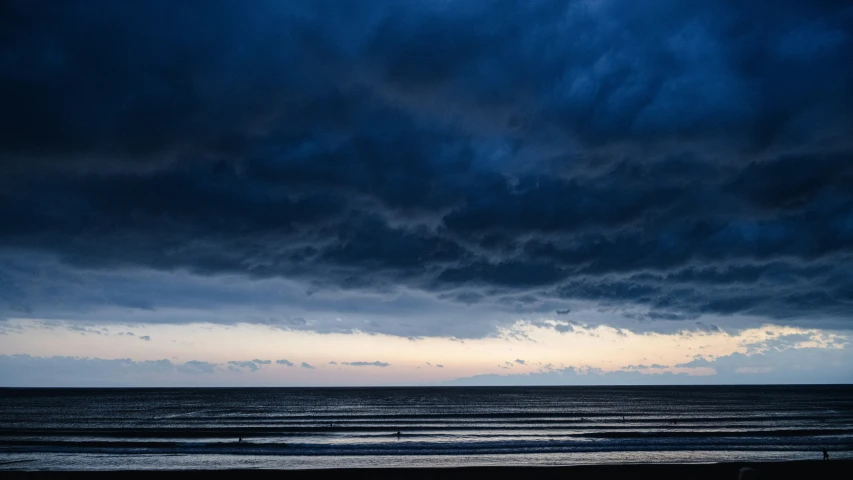 a dark ocean with some clouds and a blue sky