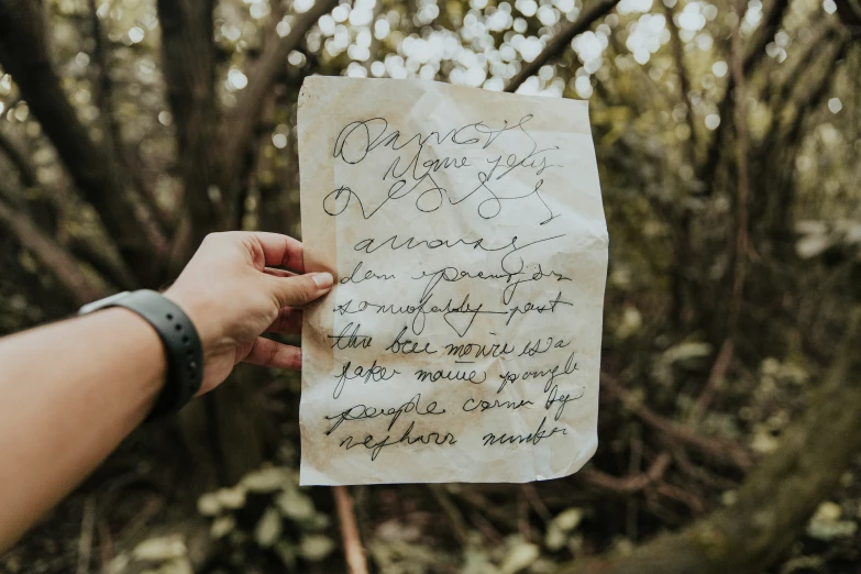 someone's hand holding a piece of paper in front of some trees