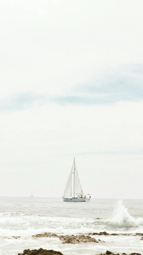 a sailboat sails across the sea as a wave crashes on rocks