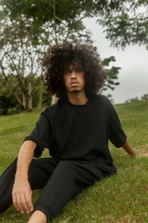 a person sitting on the grass with a bushy afro