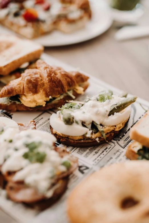 small sandwiches sit on top of newspaper next to cups