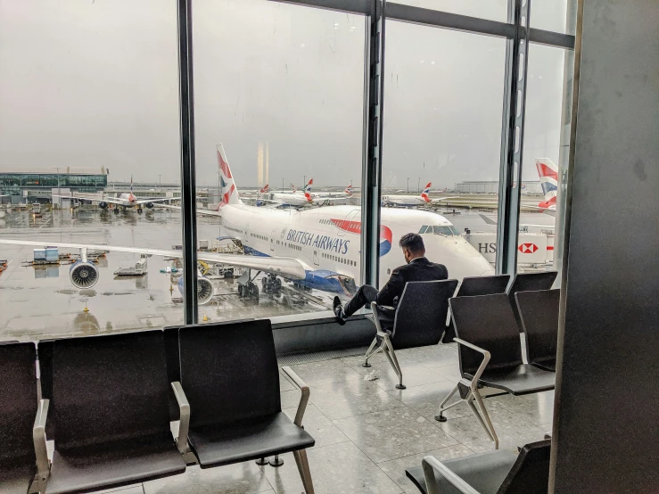 a man sits on a seat near a window watching planes