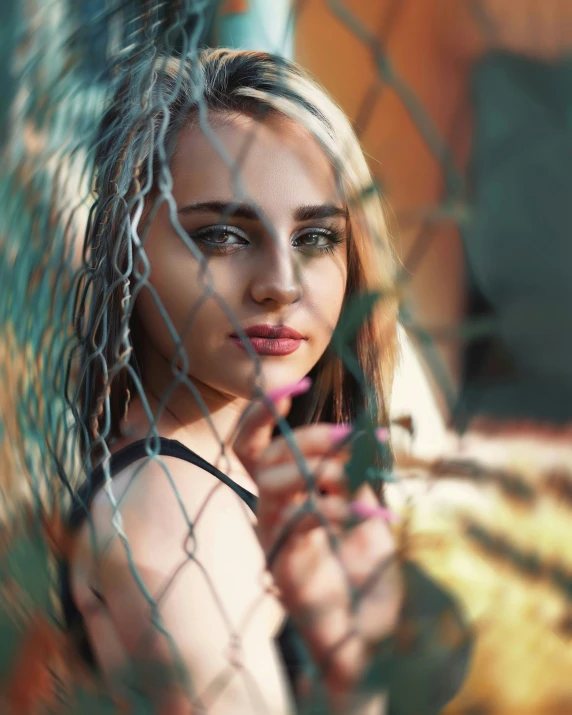 a beautiful young lady with blue eyes behind a chain link fence