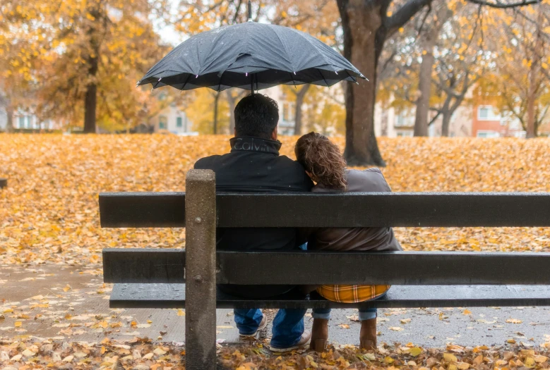 two people sitting on a bench with an umbrella