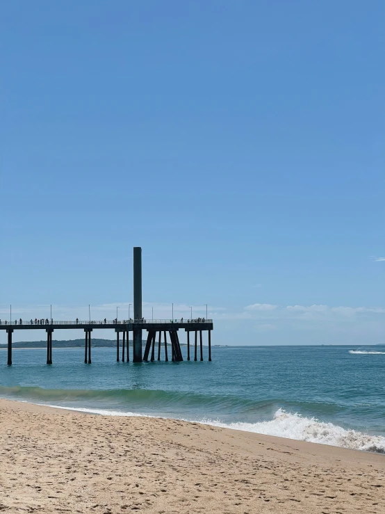 the beach is sandy and empty as people are standing on a dock