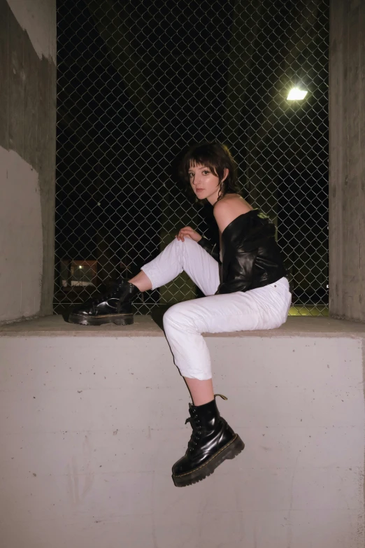 a girl in a leather jacket and leggings sits on the edge of a ledge