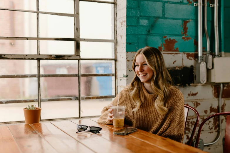 a woman is sitting at a table with a drink and cell phone