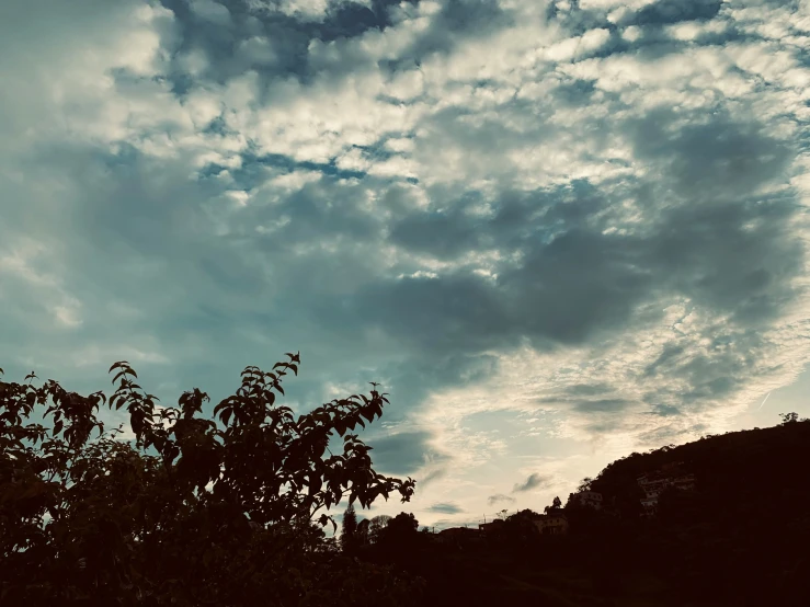 a picture of clouds, trees and the sun going down