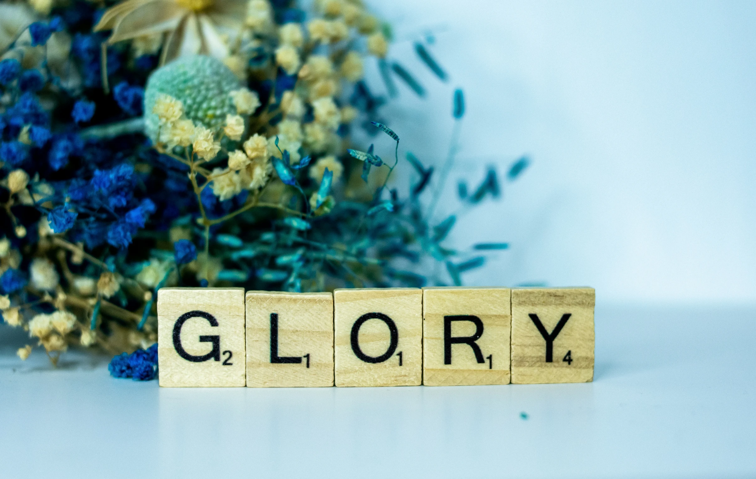 a block spelling glory on a table next to flowers