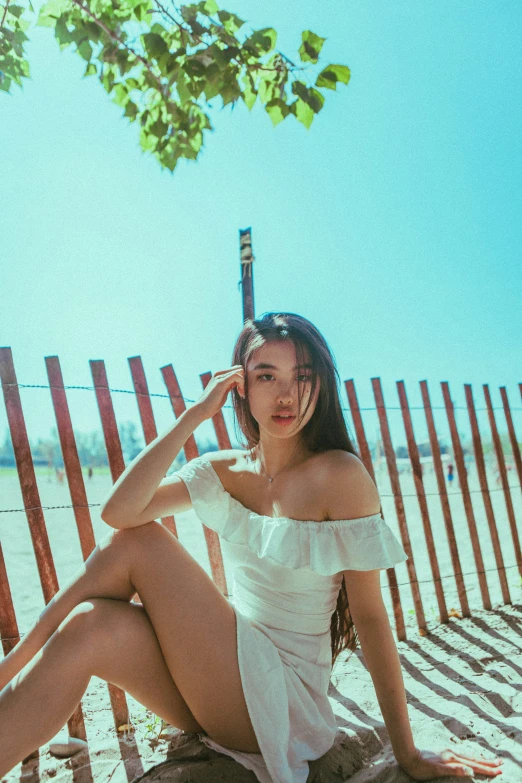 a woman sitting on top of a sandy beach next to a fence