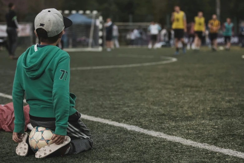 a little boy sitting on top of a soccer field