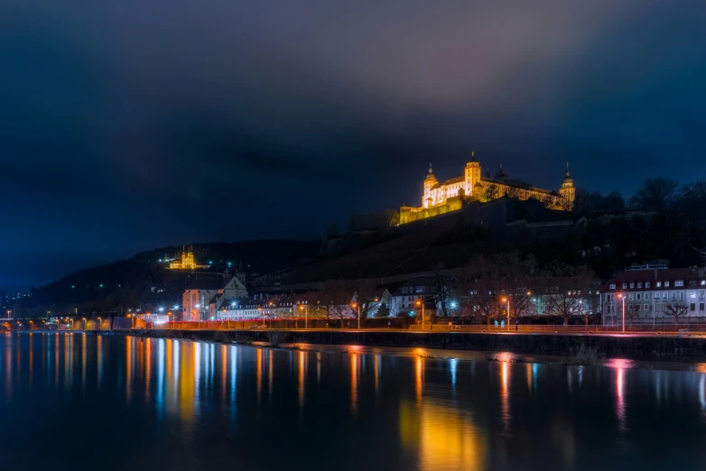 a night scene with a castle on the cliff next to a river