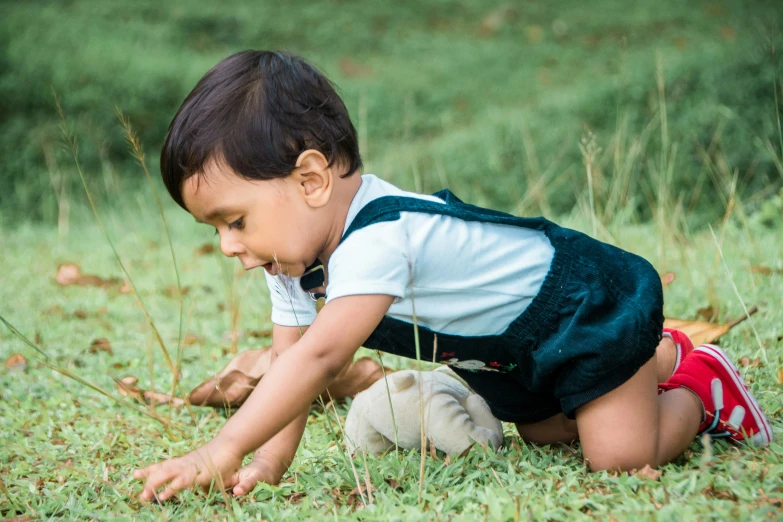 small child crawling on grass next to stuffed animal