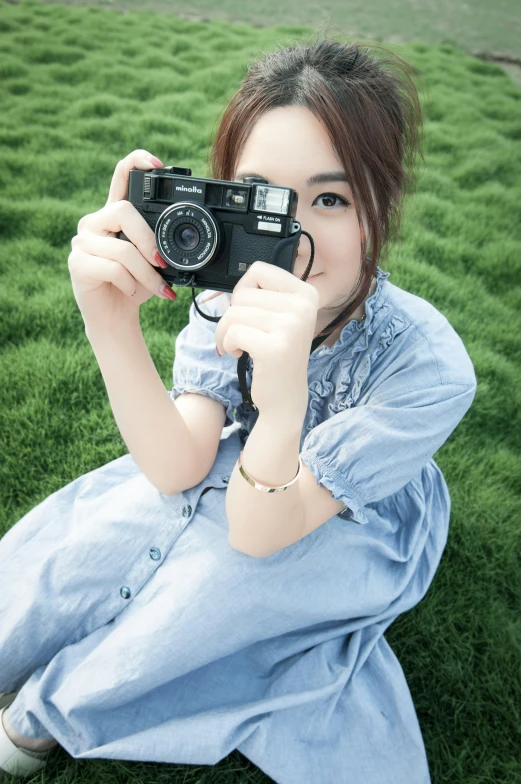 a girl holding up a camera sitting in some green grass