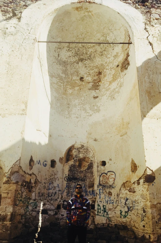 a man in a black shirt is standing near a wall that has writing on it