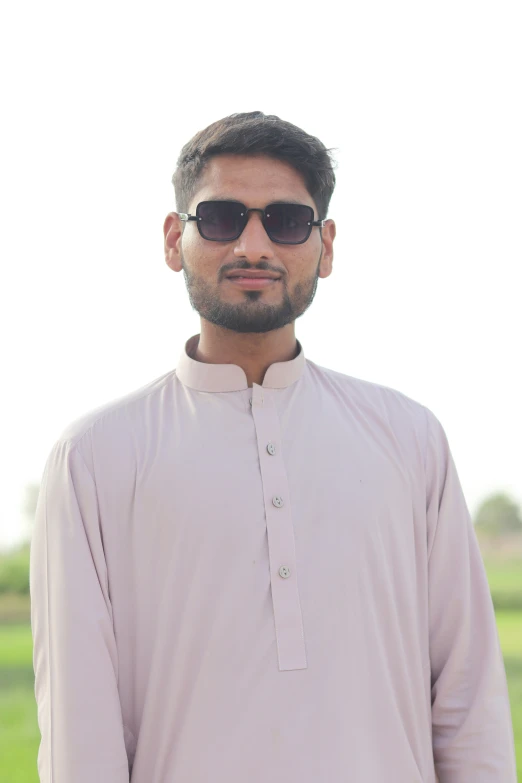 an indian man standing in front of a green field