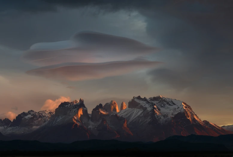 some clouds are hovering over the mountains at dusk