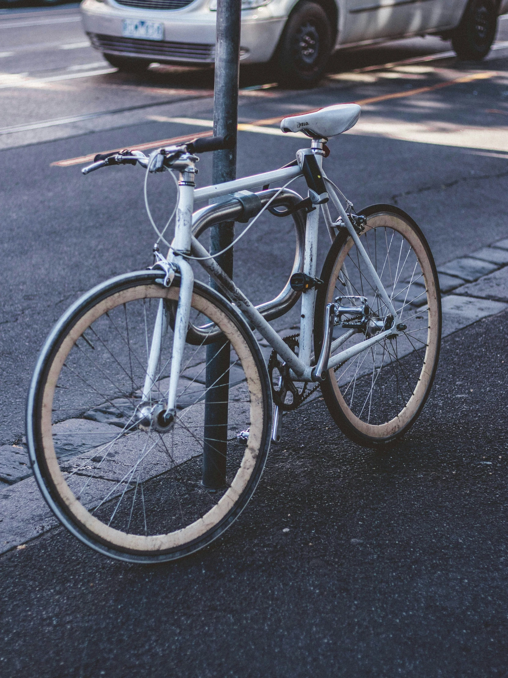 a dirty bicycle  to a pole on the sidewalk