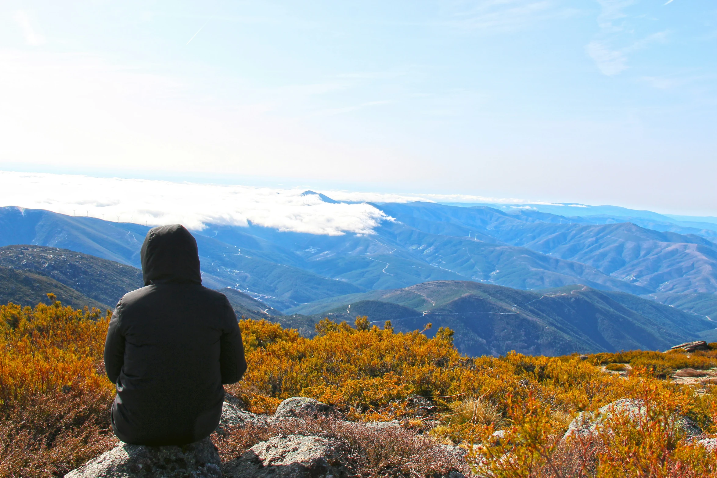 a man is standing on top of a mountain, overlooking a valley with snow covered mountains