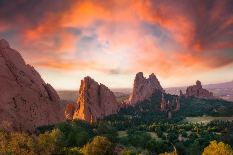 mountains, trees, and hills under an orange and blue cloudy sky