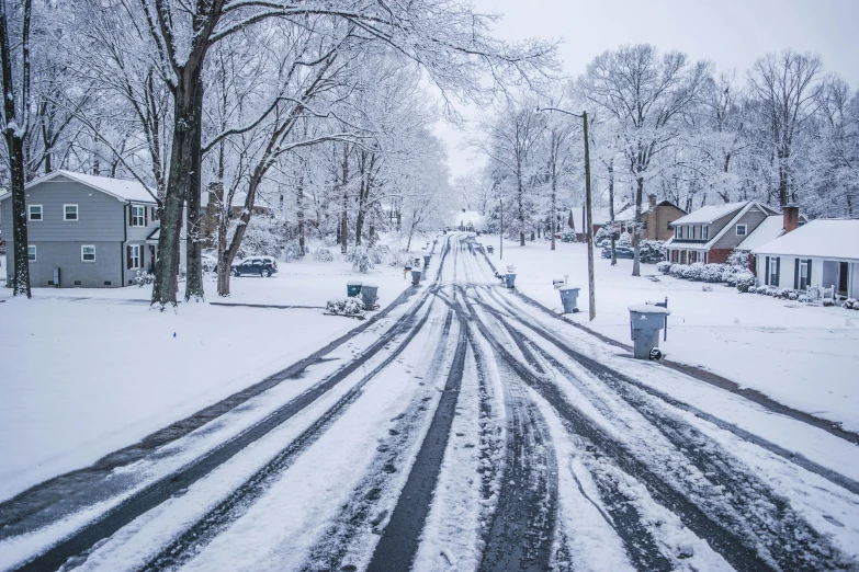 a snow covered road in a neighborhood next to a tree