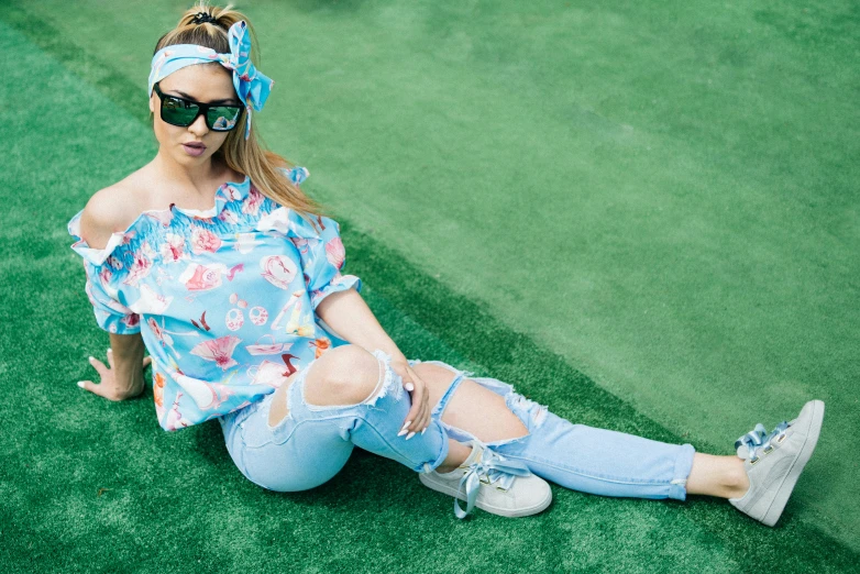 a woman wearing sunglasses and sitting on the ground with her feet crossed