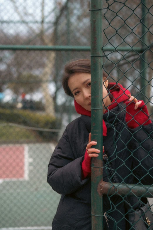 a lady looking up through a fence with her cell phone to the camera