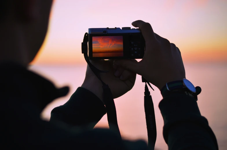 the person is looking at the sunset through their camera