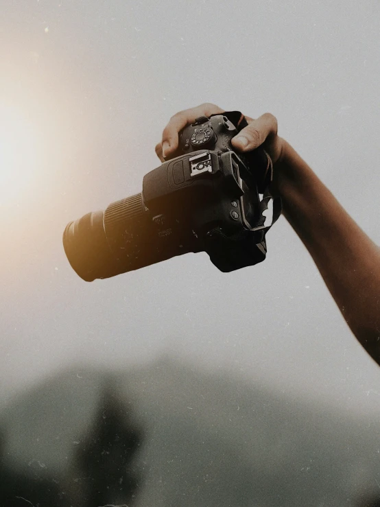 a person holding up a digital camera with the sun in the background