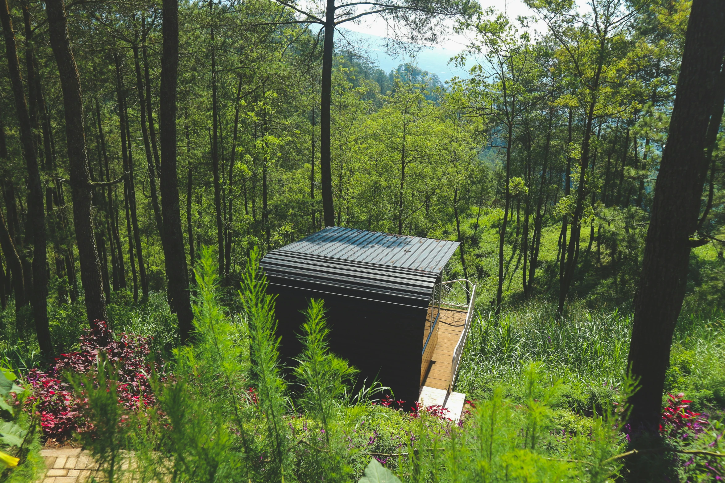 the covered outhouse is near trees and flowers