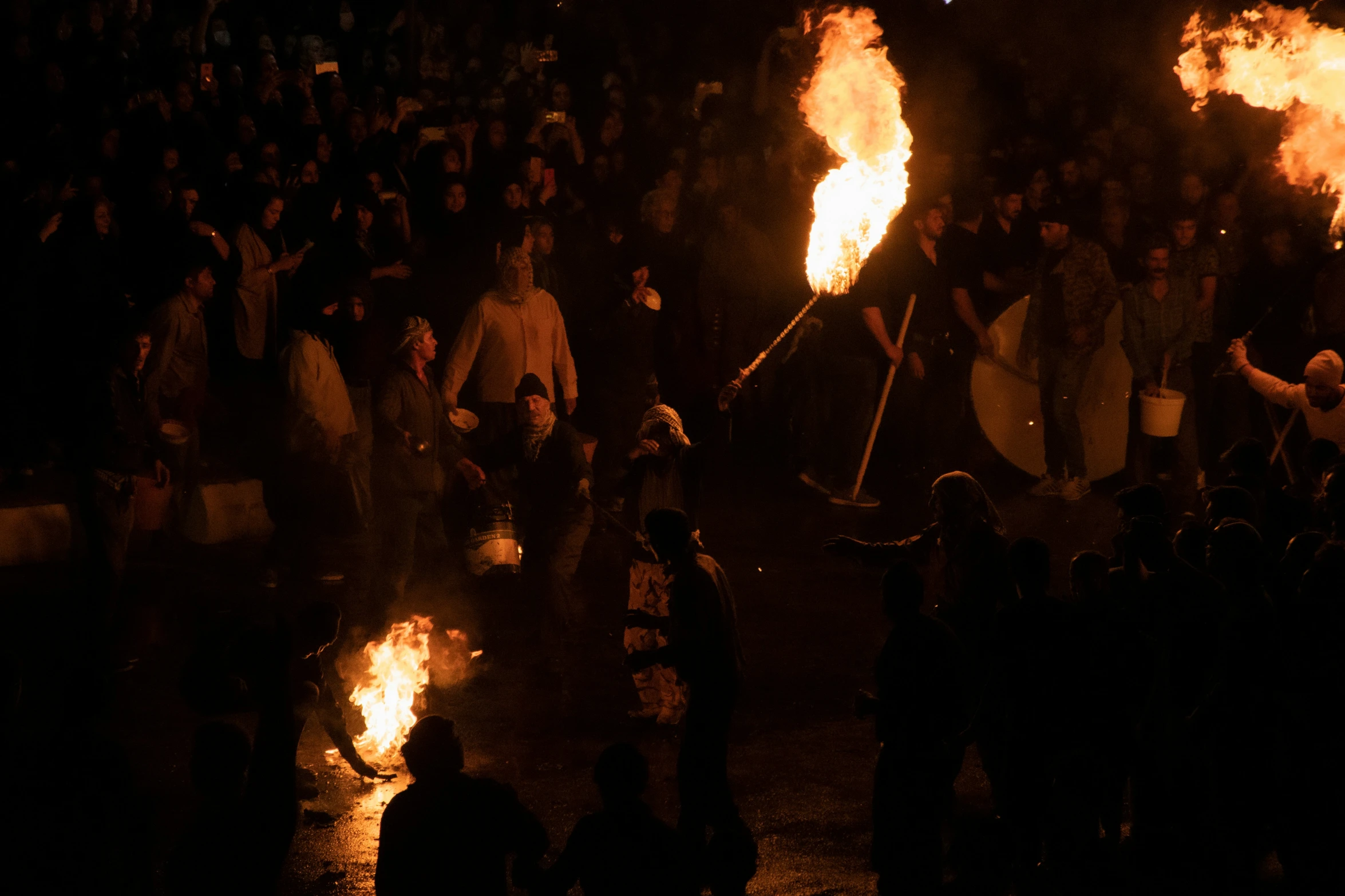 several people stand in front of a crowd of fire as their torches turn up bright