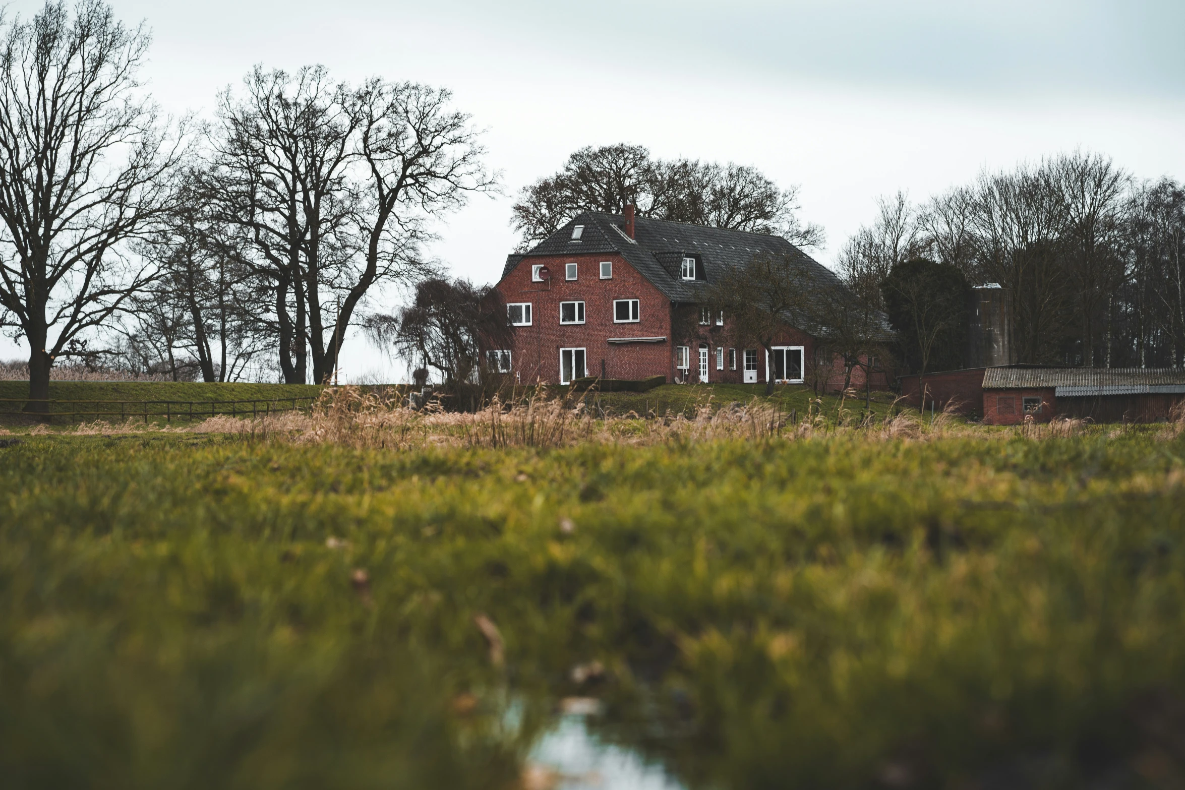 a red brick house surrounded by a lush green field