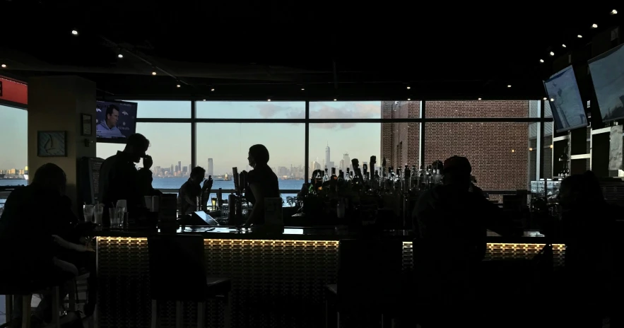 people sitting and standing at the bar, talking, in front of the city skyline