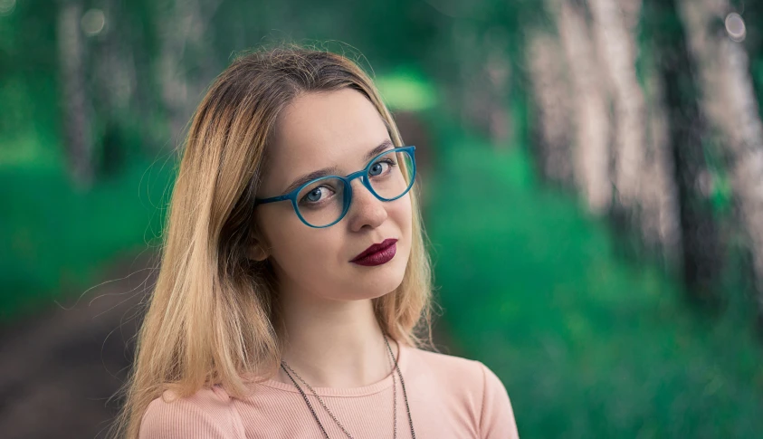 a young blonde in blue and pink glasses looking straight ahead