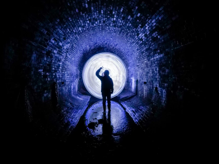 man standing in tunnel with dark lights and brick structure