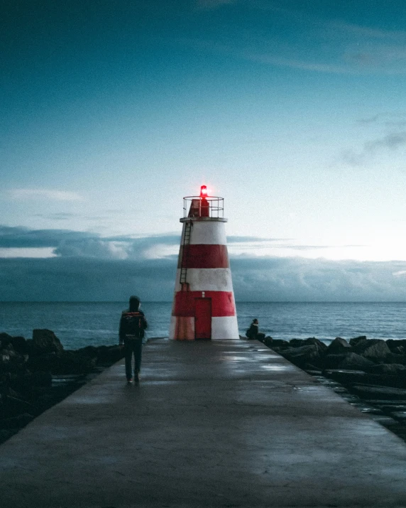 a person standing on a pier with a red and white striped lighthouse next to it