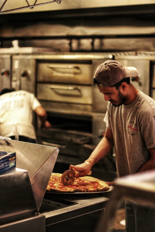 a man preparing pizza in a kitchen with another man in the background