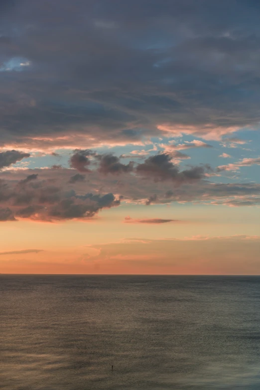 the sun is setting over the ocean with clouds in the sky