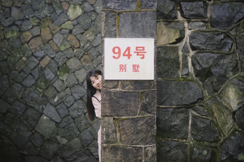 a woman is standing by a stone wall