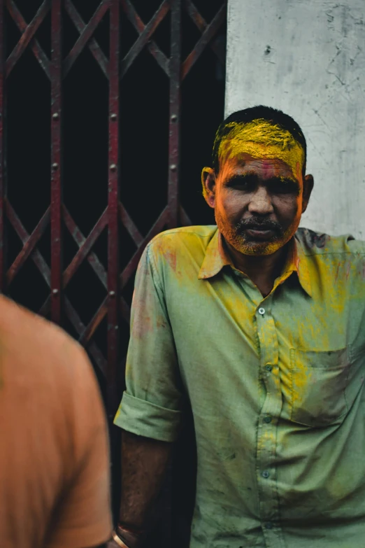 man with colored facial expression in shirt standing by fence