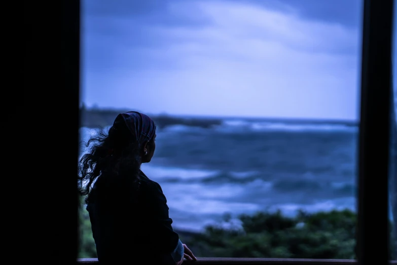 woman looking out at rough ocean from window