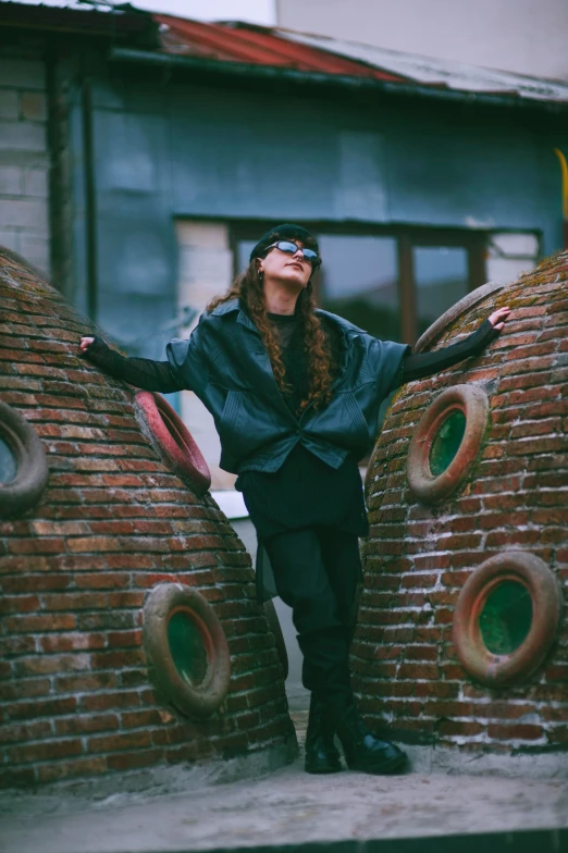 a woman wearing a black coat and holding out her hands on a brick wall