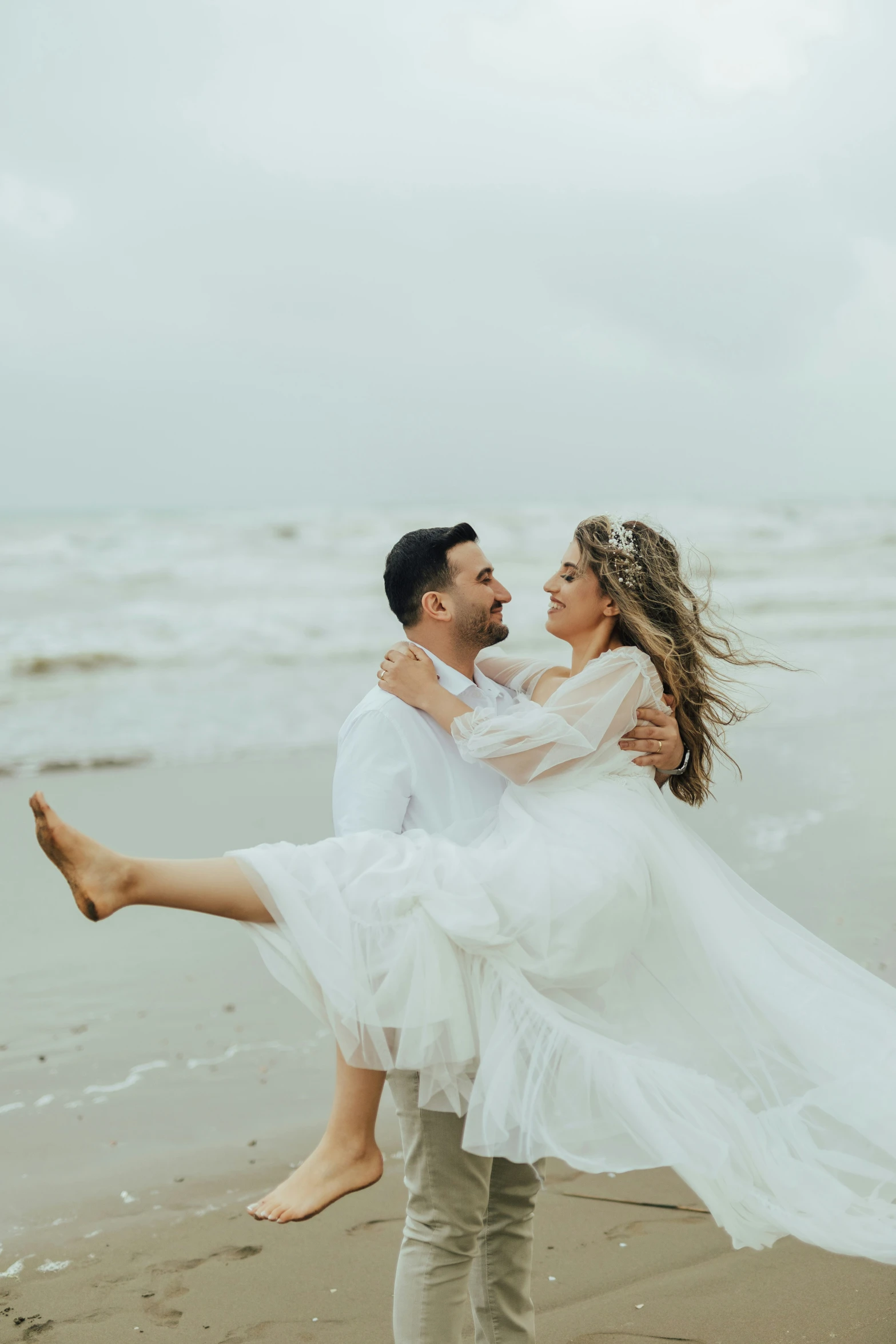 man carrying woman along on beach during wedding portraits