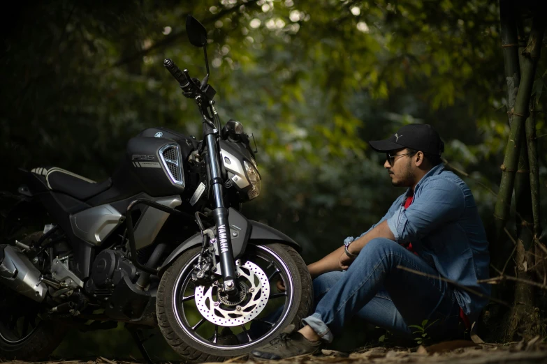 man sitting next to his motorcycle in the woods