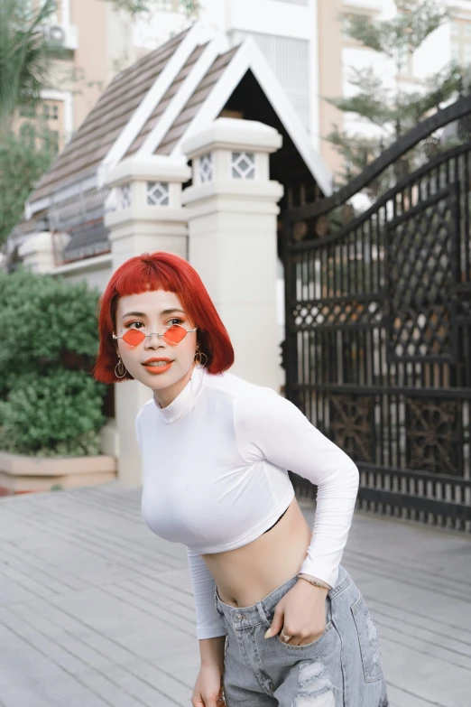 a girl with red hair wearing white shirt and jeans poses in front of a fence