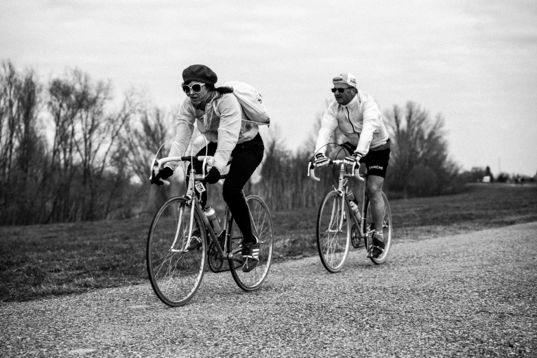 two people riding bicycles down the street in front of trees